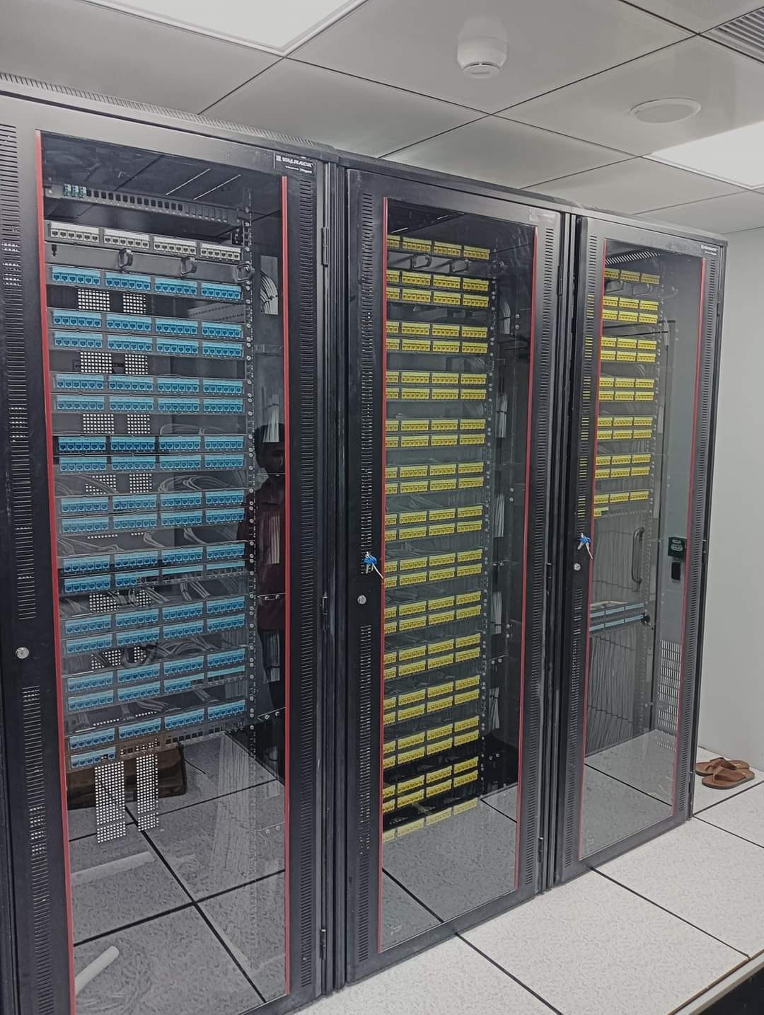 Three glass-fronted network cabinets with blue and yellow patch panels